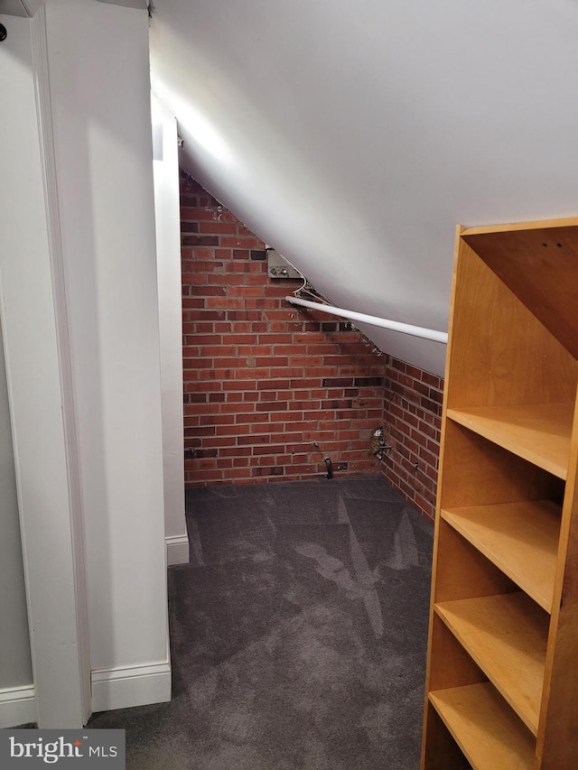 bonus room with dark colored carpet, lofted ceiling, and brick wall