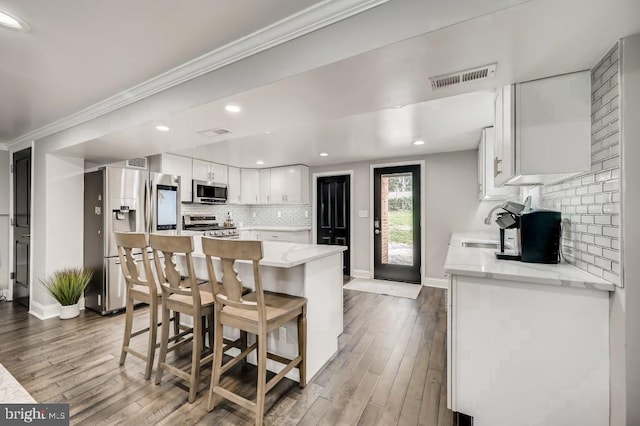 kitchen with hardwood / wood-style floors, white cabinets, decorative backsplash, ornamental molding, and stainless steel appliances