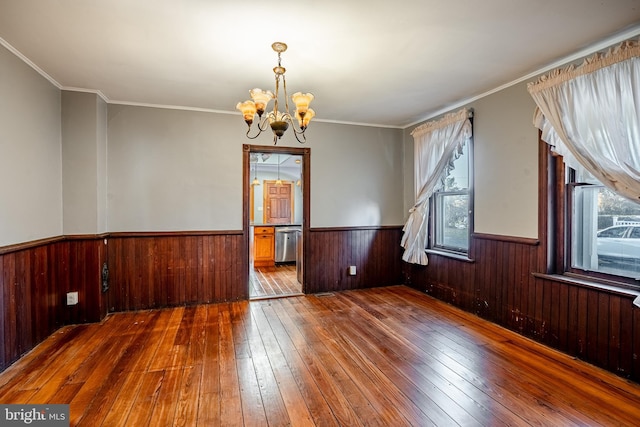 spare room featuring wooden walls, ornamental molding, a notable chandelier, and hardwood / wood-style flooring