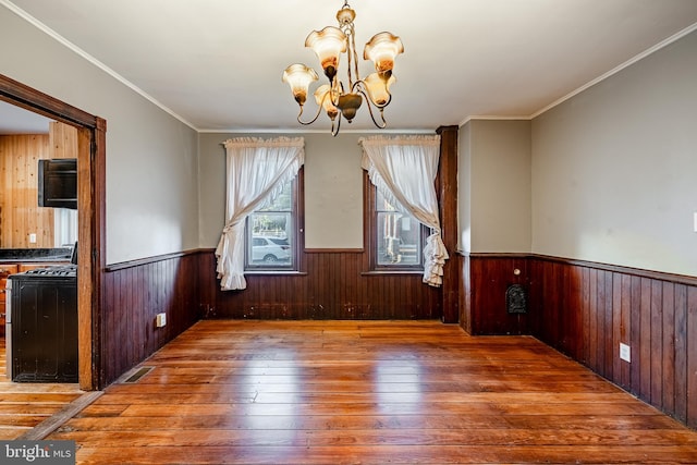 unfurnished dining area with a chandelier, wood-type flooring, crown molding, and wood walls