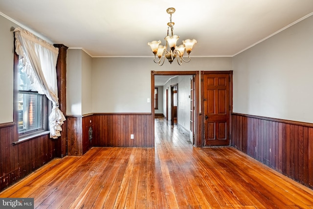 spare room with wooden walls, an inviting chandelier, ornamental molding, and hardwood / wood-style flooring