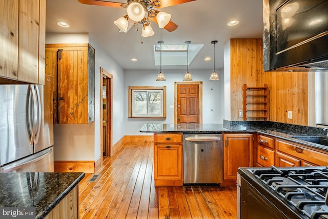 kitchen with ceiling fan, hanging light fixtures, stainless steel appliances, dark stone counters, and light wood-type flooring