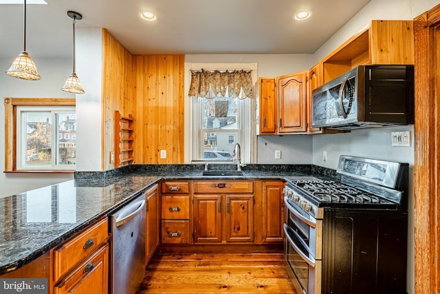 kitchen featuring sink, stainless steel appliances, dark stone countertops, pendant lighting, and light wood-type flooring