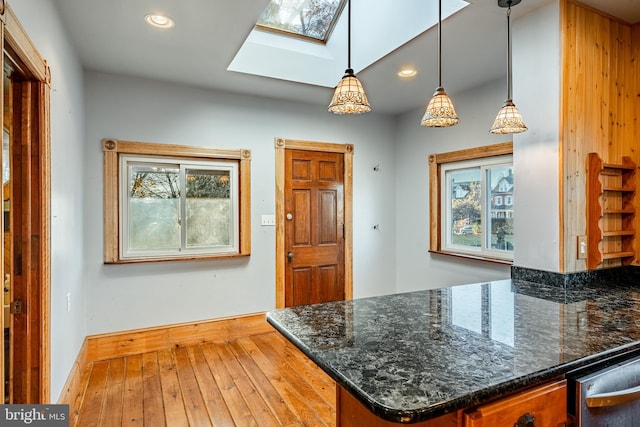 kitchen featuring hardwood / wood-style flooring, hanging light fixtures, dark stone counters, and a skylight