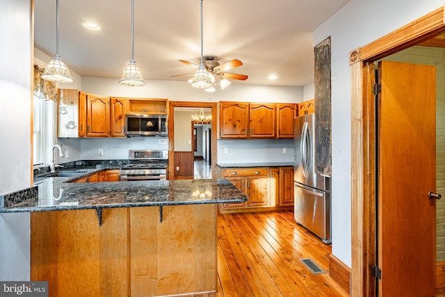 kitchen featuring kitchen peninsula, appliances with stainless steel finishes, sink, decorative light fixtures, and light hardwood / wood-style flooring