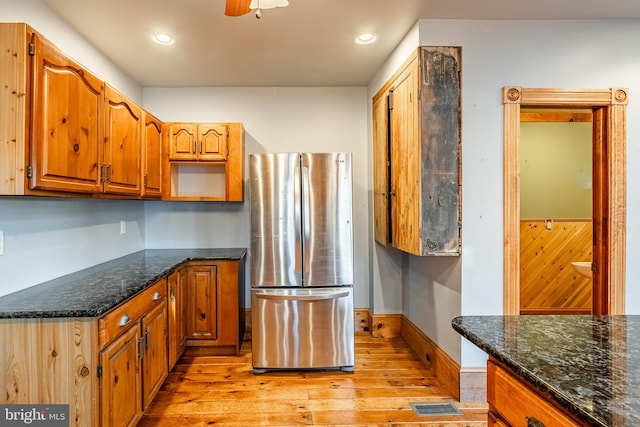 kitchen with stainless steel fridge, light hardwood / wood-style floors, ceiling fan, and dark stone counters