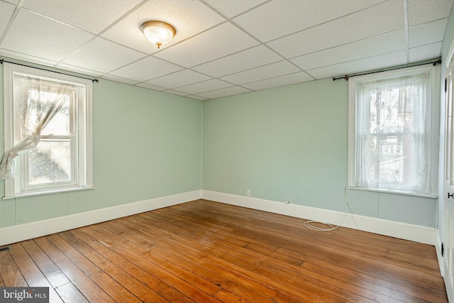 empty room with a wealth of natural light, hardwood / wood-style floors, and a drop ceiling