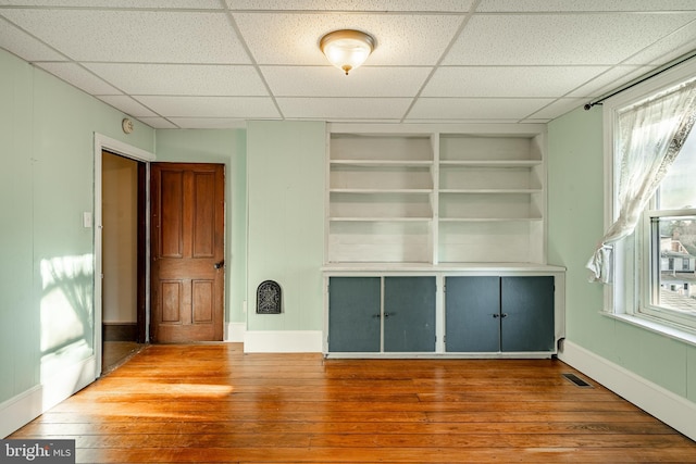 interior space featuring a paneled ceiling, built in features, and hardwood / wood-style flooring