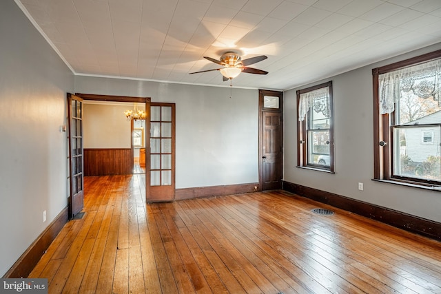 spare room featuring french doors, wood walls, hardwood / wood-style flooring, ceiling fan with notable chandelier, and ornamental molding