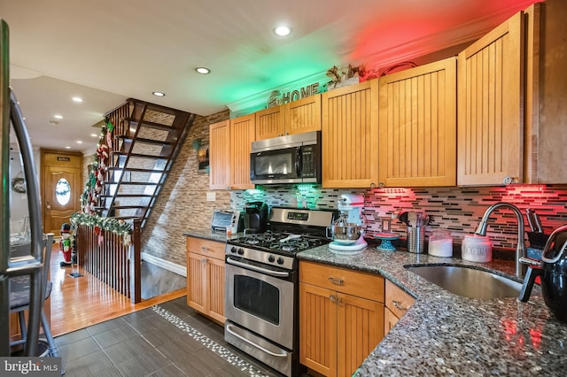 kitchen featuring decorative backsplash, appliances with stainless steel finishes, dark stone counters, sink, and dark hardwood / wood-style floors