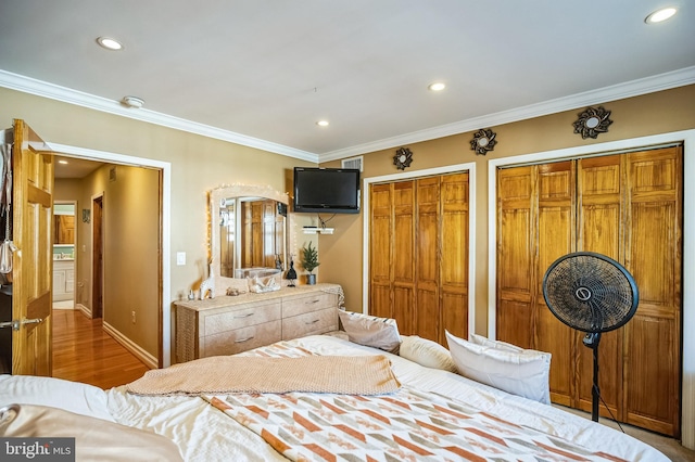 bedroom featuring crown molding, wood-type flooring, and two closets