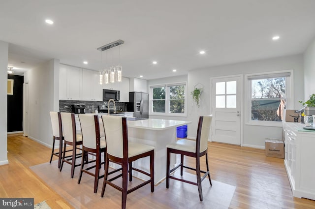 kitchen featuring white cabinets, hanging light fixtures, appliances with stainless steel finishes, and light hardwood / wood-style flooring