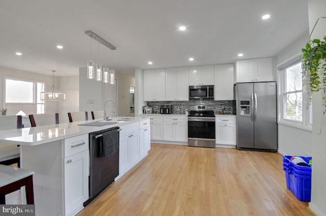 kitchen featuring white cabinetry, hanging light fixtures, stainless steel appliances, and light hardwood / wood-style floors