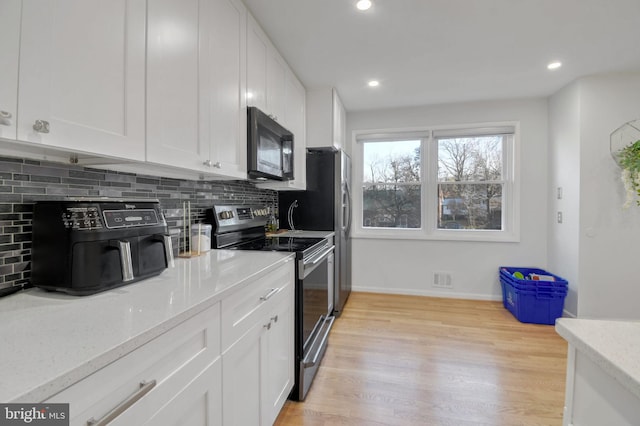 kitchen featuring light stone countertops, light hardwood / wood-style flooring, white cabinetry, and stainless steel electric range