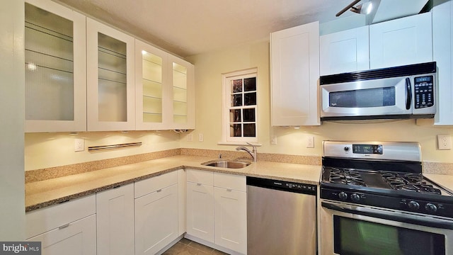 kitchen featuring appliances with stainless steel finishes, light stone counters, sink, light tile patterned floors, and white cabinets