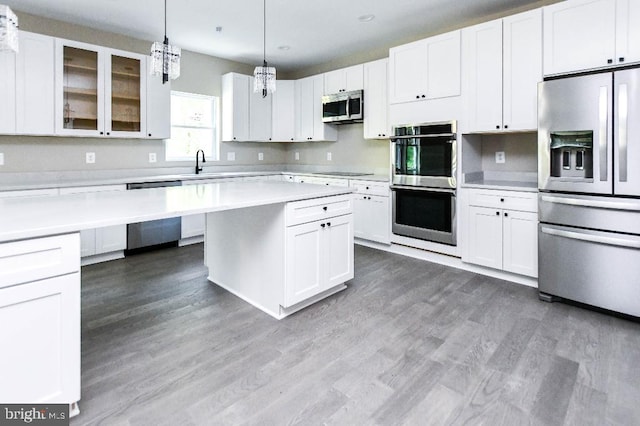 kitchen with appliances with stainless steel finishes, white cabinetry, and hanging light fixtures