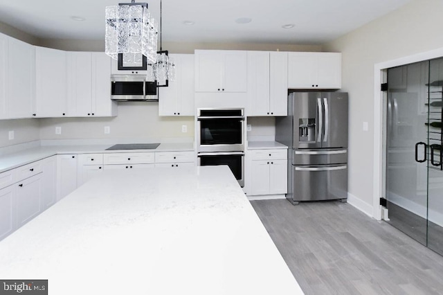 kitchen with pendant lighting, light wood-type flooring, white cabinetry, and appliances with stainless steel finishes