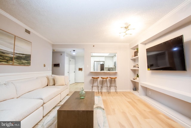 living room featuring crown molding, built in features, a textured ceiling, and light hardwood / wood-style flooring