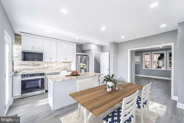 kitchen featuring a center island, light hardwood / wood-style flooring, light stone counters, white cabinetry, and stainless steel appliances