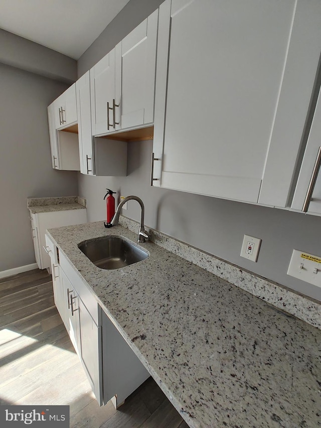 kitchen with light stone counters, dark hardwood / wood-style floors, white cabinetry, and sink