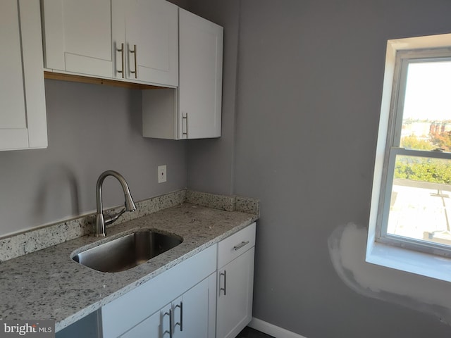 kitchen featuring light stone counters, sink, and white cabinets