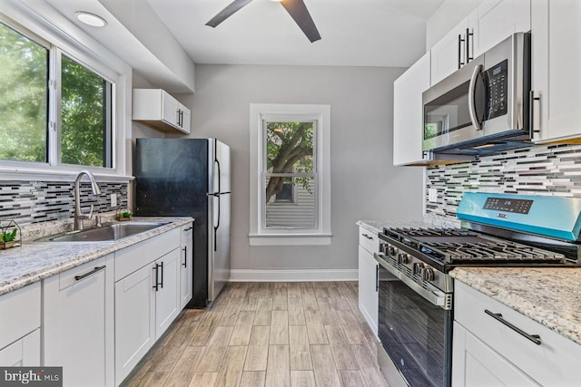 kitchen with white cabinets, stainless steel appliances, light stone countertops, and sink