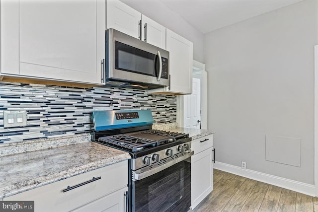 kitchen with light stone countertops, appliances with stainless steel finishes, light wood-type flooring, decorative backsplash, and white cabinetry