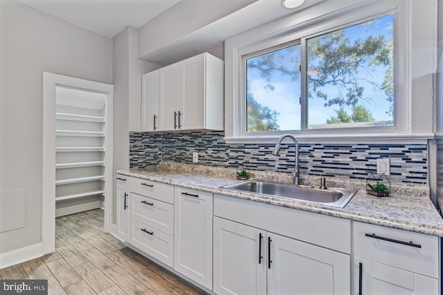 kitchen with light stone countertops, backsplash, sink, white cabinets, and light hardwood / wood-style floors