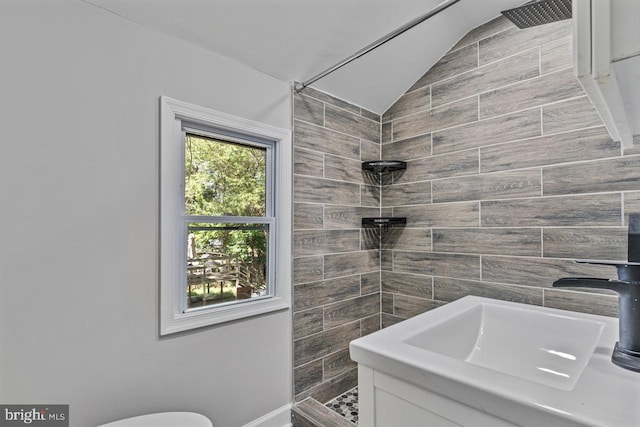 bathroom with tiled shower, vaulted ceiling, toilet, and sink