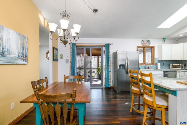 dining room with lofted ceiling with skylight, dark hardwood / wood-style flooring, a chandelier, and sink