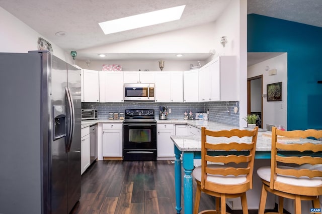 kitchen featuring decorative backsplash, dark hardwood / wood-style flooring, vaulted ceiling with skylight, stainless steel appliances, and white cabinetry