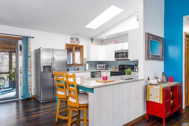 kitchen featuring white cabinets, vaulted ceiling with skylight, tasteful backsplash, kitchen peninsula, and stainless steel appliances