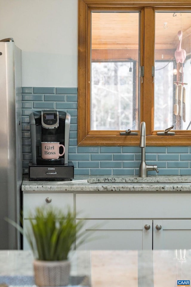 room details with decorative backsplash, light stone counters, white cabinetry, and stainless steel refrigerator