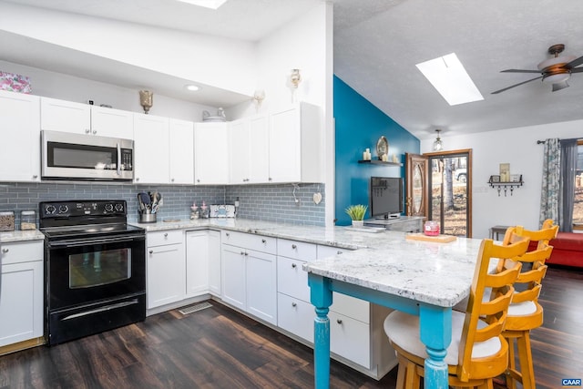 kitchen with black / electric stove, lofted ceiling with skylight, kitchen peninsula, and white cabinets