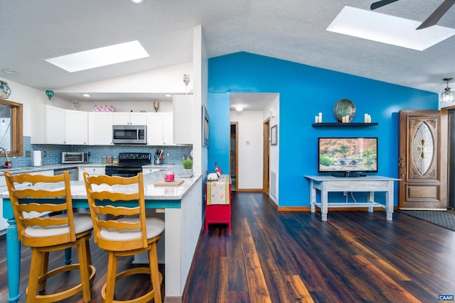 kitchen with a kitchen bar, appliances with stainless steel finishes, decorative backsplash, vaulted ceiling with skylight, and white cabinets