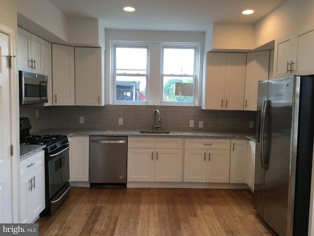 kitchen with light stone counters, stainless steel appliances, sink, light hardwood / wood-style flooring, and white cabinets