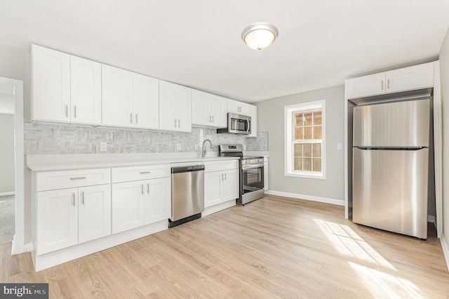 kitchen with decorative backsplash, appliances with stainless steel finishes, light wood-type flooring, sink, and white cabinets