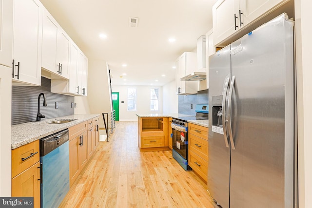 kitchen featuring wall chimney range hood, light hardwood / wood-style flooring, light stone countertops, appliances with stainless steel finishes, and white cabinetry