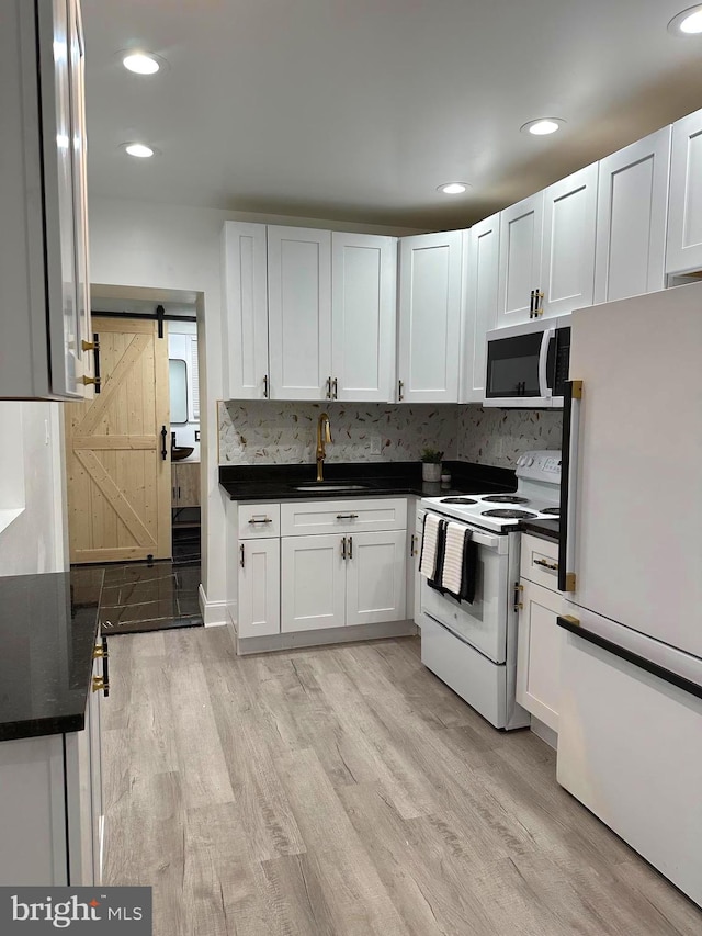 kitchen featuring white appliances, light wood-type flooring, a barn door, and white cabinetry