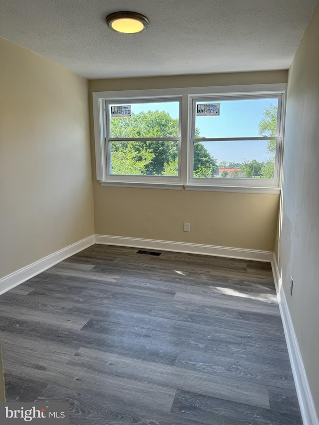 unfurnished room with a textured ceiling, dark wood-type flooring, and a healthy amount of sunlight