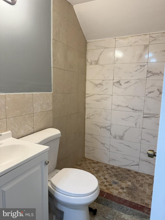 bathroom with vanity, vaulted ceiling, toilet, tiled shower, and tile walls