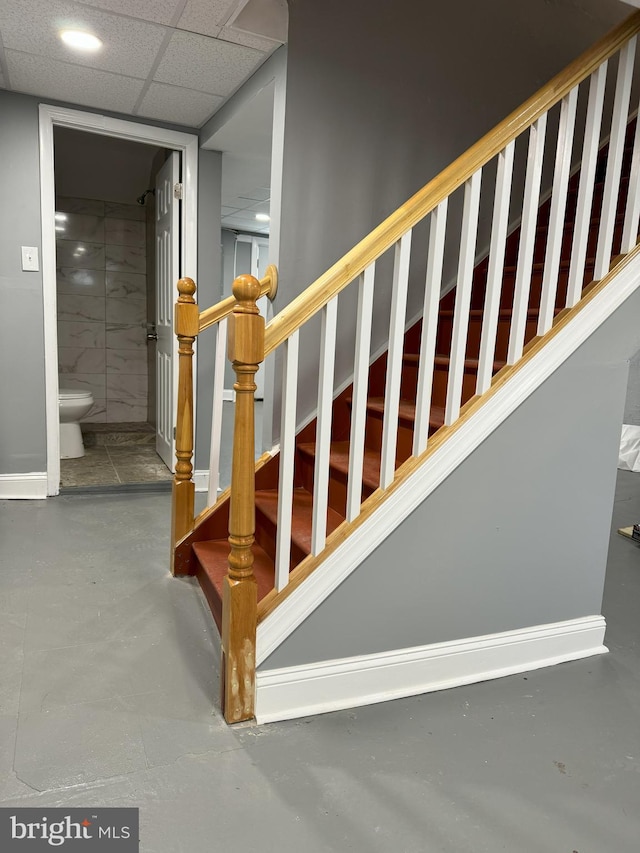 staircase featuring a paneled ceiling and concrete flooring