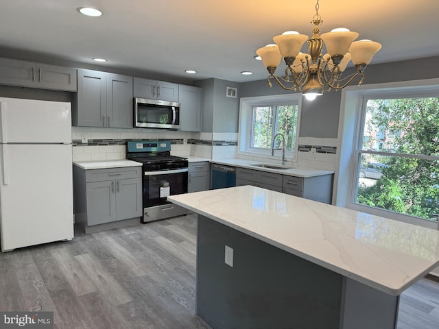 kitchen with decorative light fixtures, sink, stainless steel appliances, and a wealth of natural light