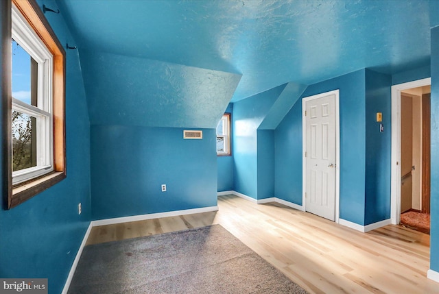 bonus room featuring a textured ceiling, wood-type flooring, and lofted ceiling