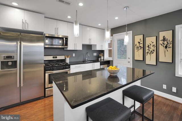 kitchen with white cabinets, hanging light fixtures, appliances with stainless steel finishes, a kitchen island, and a breakfast bar area