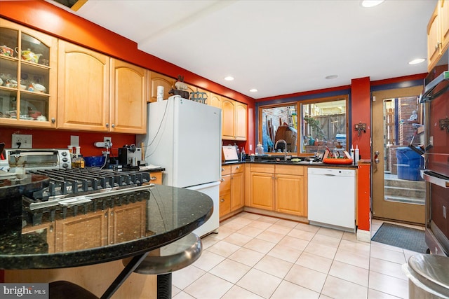 kitchen with dark stone countertops, sink, light tile patterned floors, and white appliances