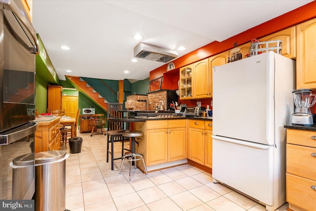 kitchen featuring white fridge, a breakfast bar area, and light tile patterned flooring