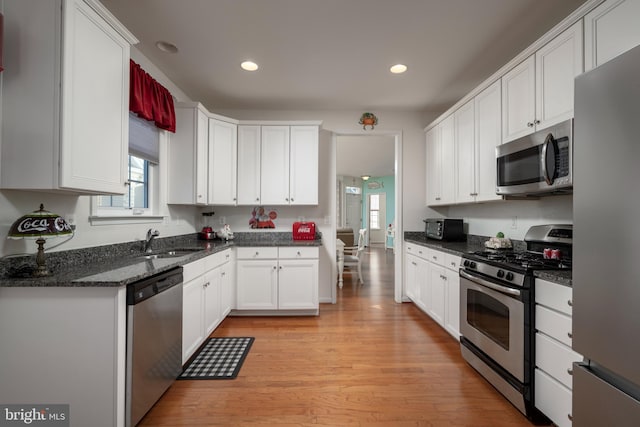 kitchen featuring sink, dark stone countertops, appliances with stainless steel finishes, white cabinets, and light wood-type flooring