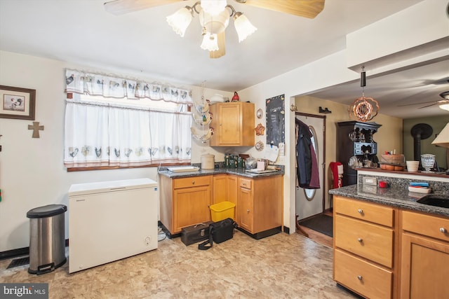 kitchen featuring ceiling fan, refrigerator, and dark stone countertops