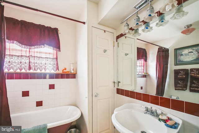 bathroom featuring plenty of natural light, a tub to relax in, sink, and tile walls